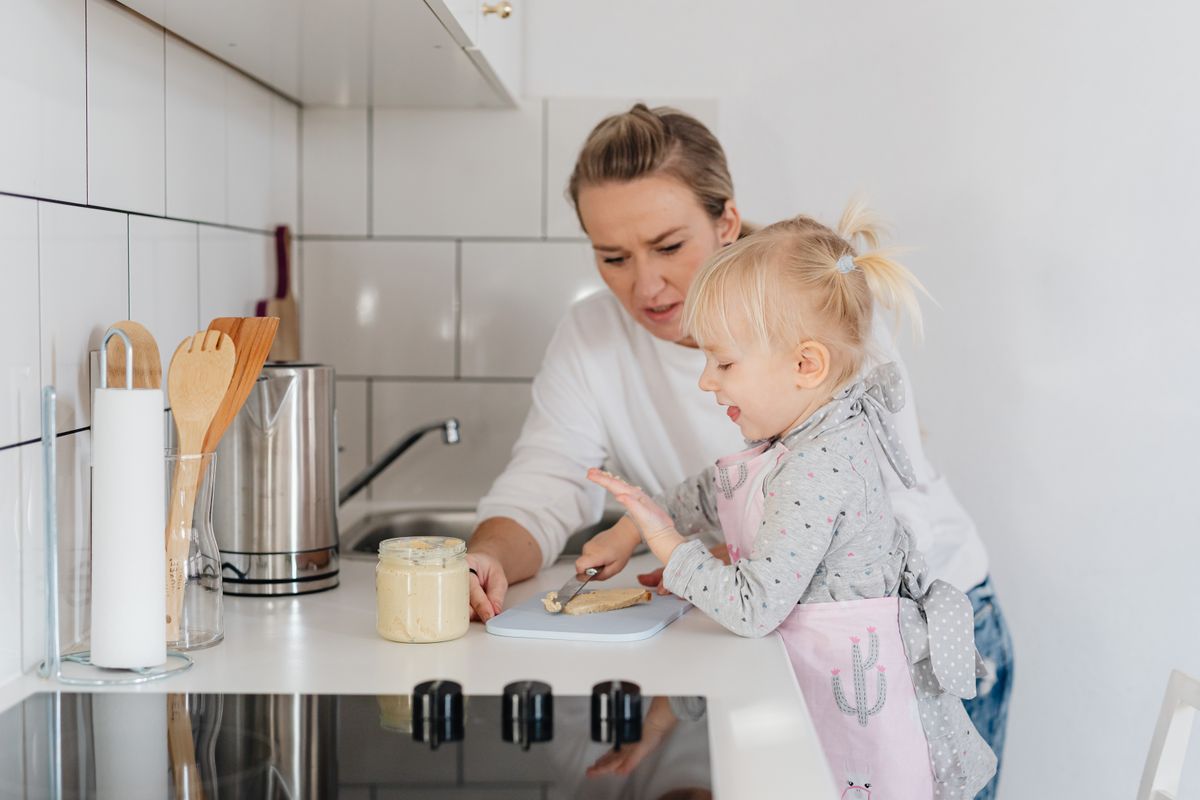 A mother and child wearing aprons preparing food in a cozy kitchen. Eine Mutter und ein Kind in Schürzen bereiten in einer gemütlichen Küche Essen zu.