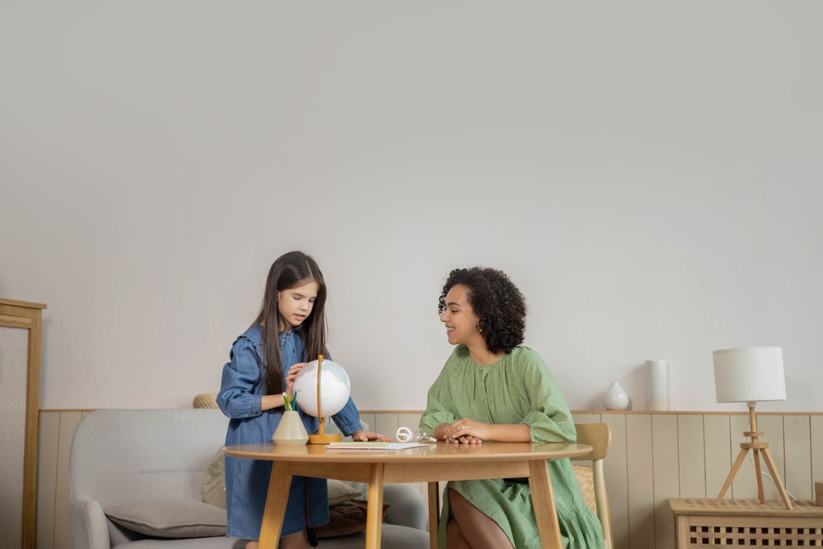 A teacher and student engage in a geography lesson with a globe in a cozy indoor setting. A teacher and student engage in a geography lesson with a globe in a cozy indoor setting.