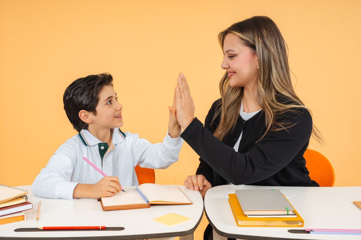 A teacher and student exchange a high-five in a classroom, fostering a positive learning environment. A teacher and student exchange a high-five in a classroom, fostering a positive learning environment.