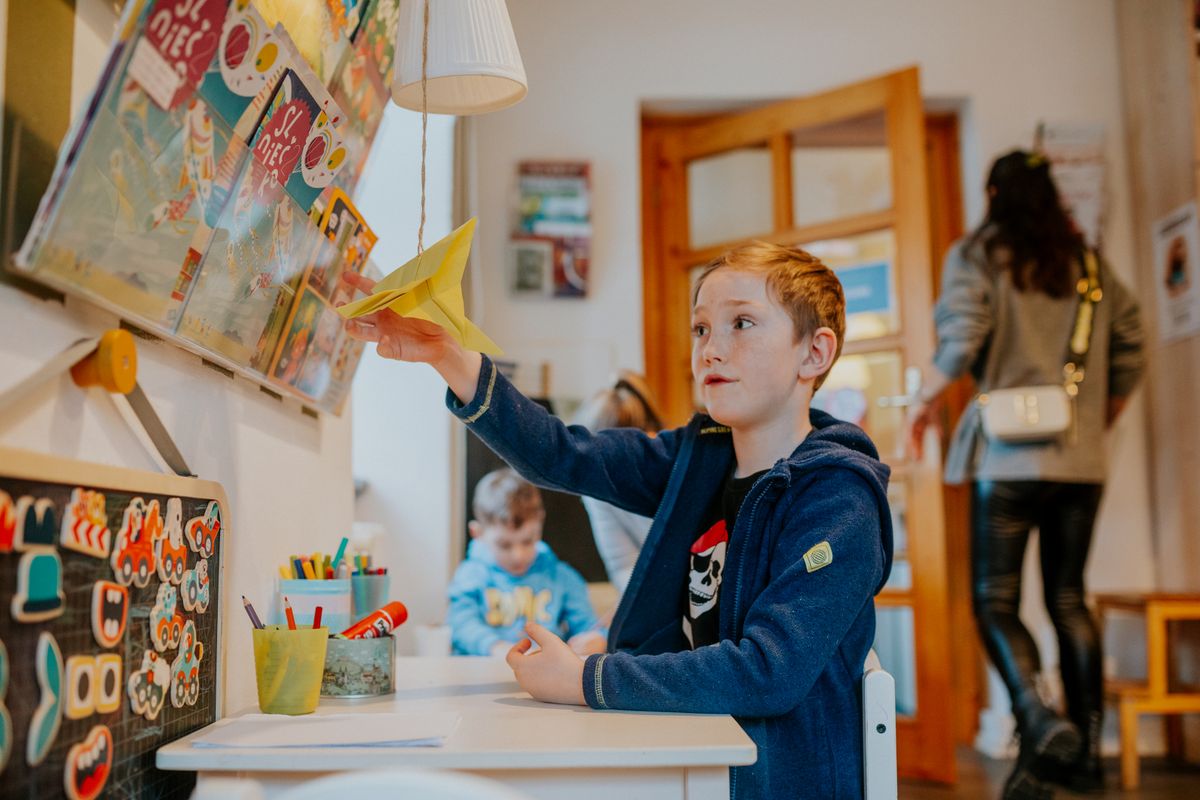 A young boy enjoying a creative activity with a paper airplane in a lively classroom setting. A young boy enjoying a creative activity with a paper airplane in a lively classroom setting.