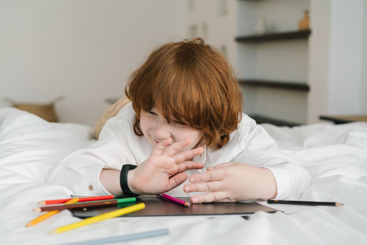 A young redheaded boy lying on a bed, playing with colored pencils indoors, expressing creativity. A young redheaded boy lying on a bed, playing with colored pencils indoors, expressing creativity.