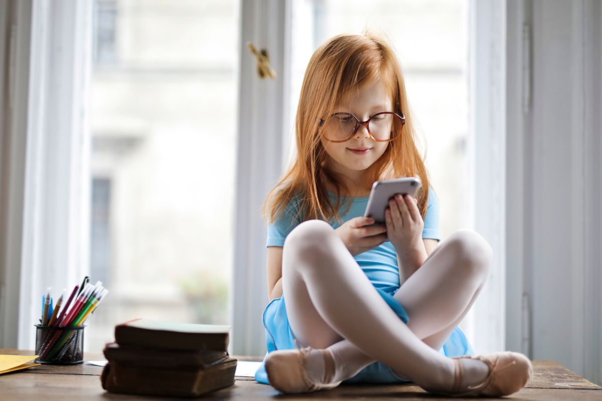 Photo by Andrea Piacquadio on Pexels Entzückendes rothaariges Mädchen mit Brille, das ein Smartphone in einem gemütlichen Raum benutzt und neben Büchern sitzt. - Foto von Andrea Piacquadio auf Pexels