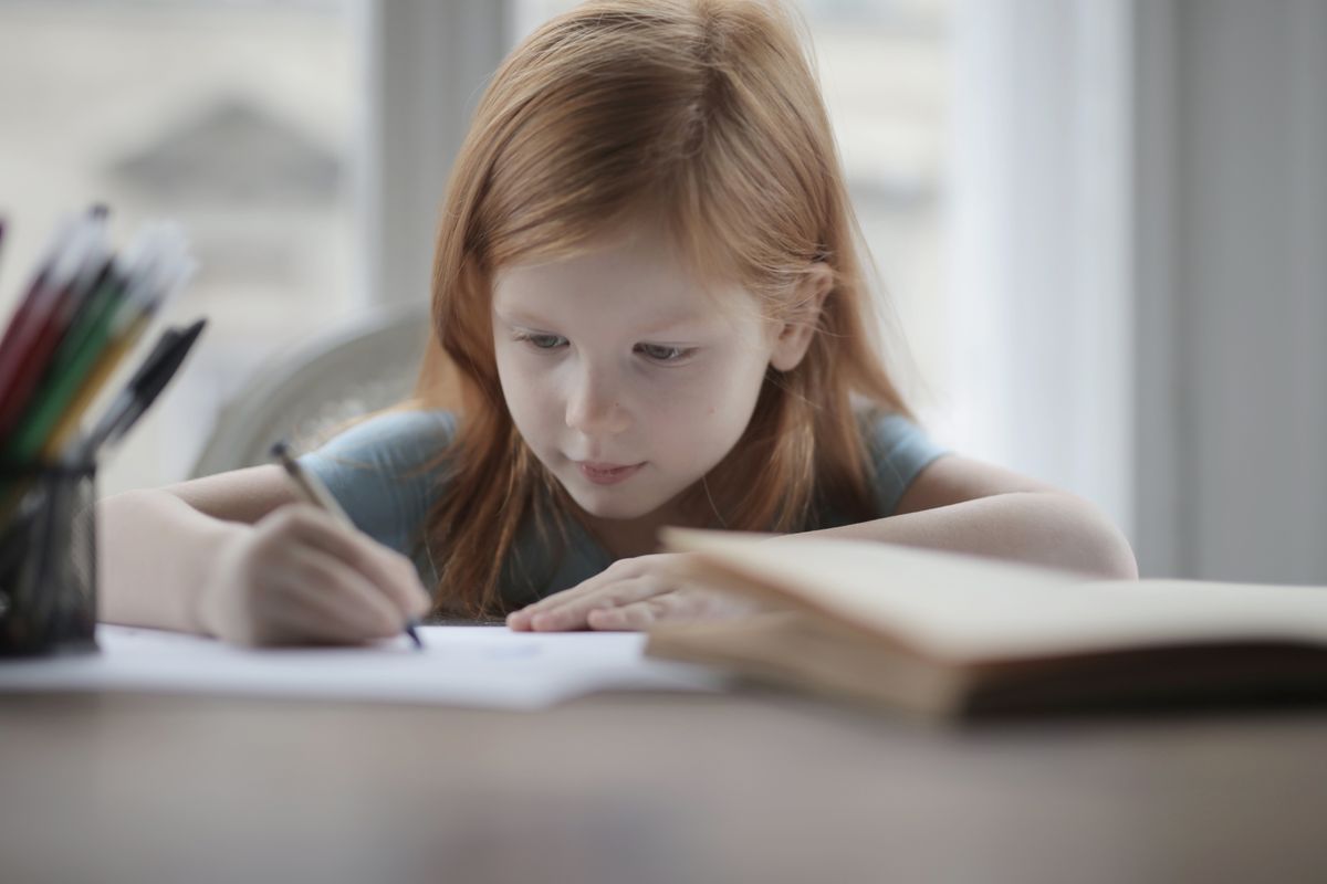 Photo by Andrea Piacquadio on Pexels Adorable positive preschool child with red hair in casual wear sitting at table with book and pens or pencils while making exercise on paper sheet against blurred window - Photo by Andrea Piacquadio on Pexels