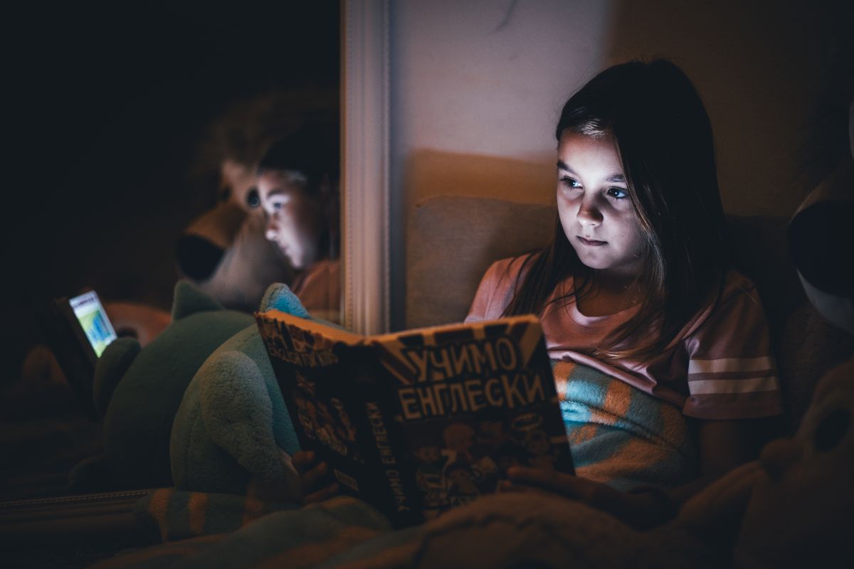 Photo by Boris Hamer on Pexels A young girl reads a book under dim light, reflecting a quiet bedtime atmosphere. - Photo by Boris Hamer on Pexels