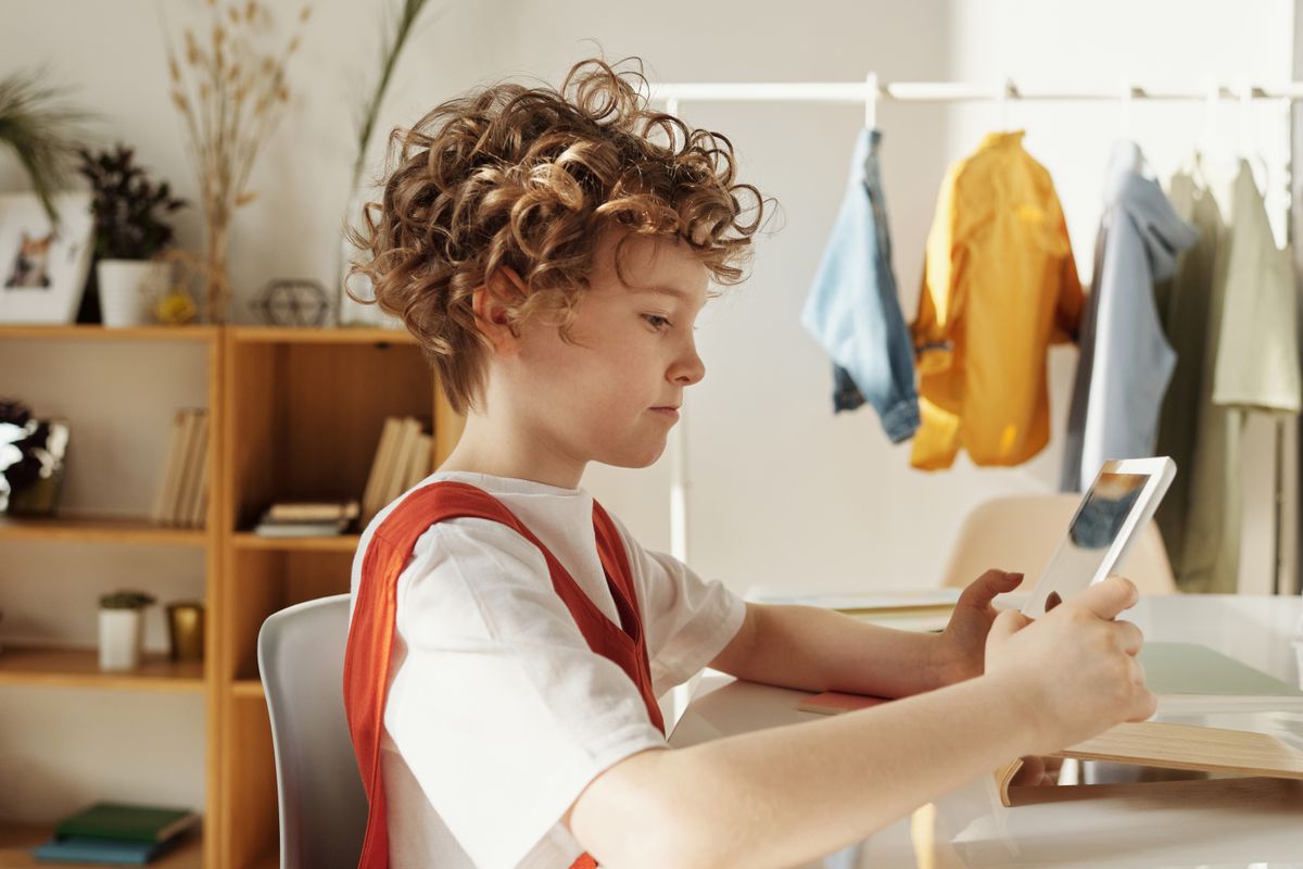Child focused on using a tablet indoors, engaging in distance learning activities. Das Kind konzentrierte sich auf die Verwendung eines Tablets im Innenbereich und nahm an Fernunterrichtsaktivitäten teil.