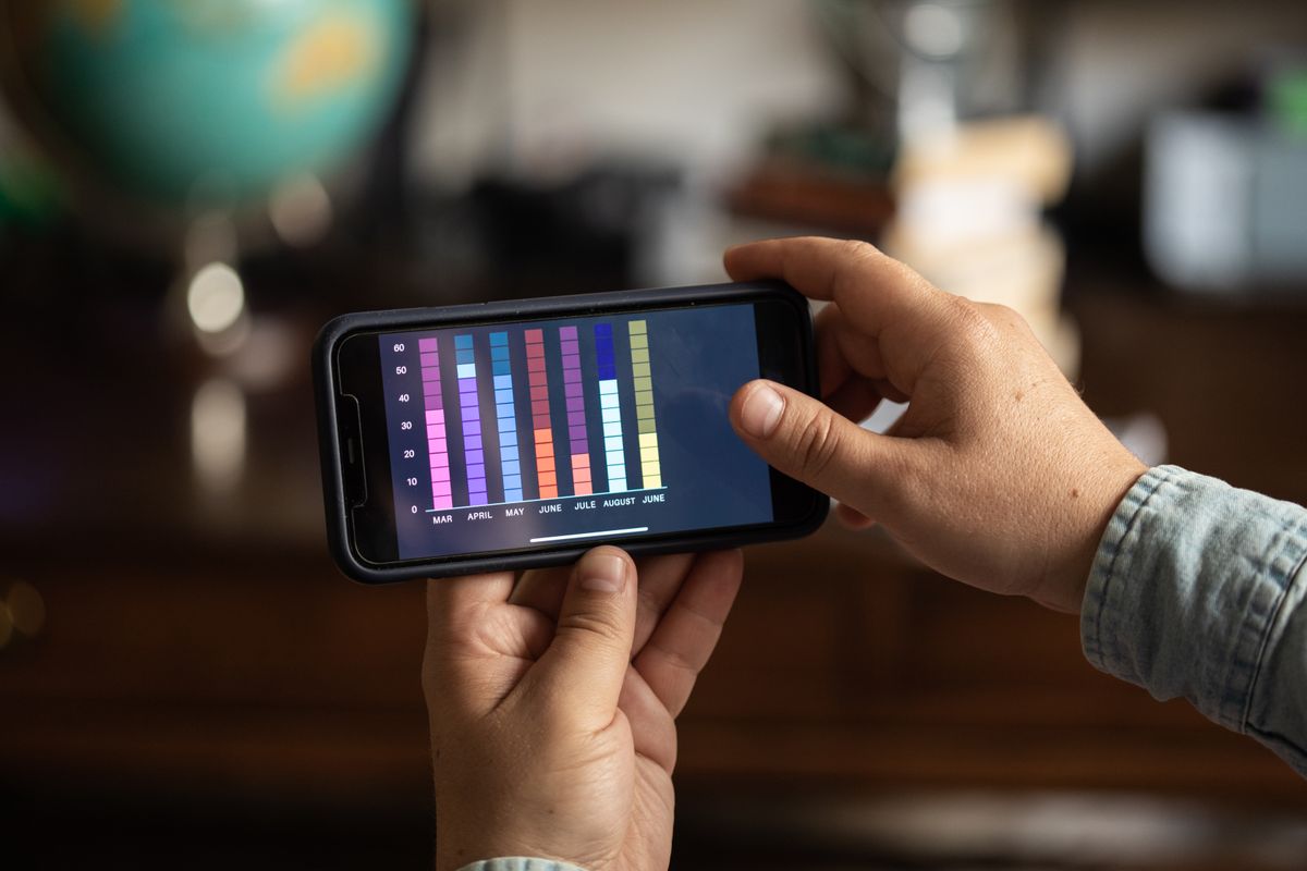 Close-up of hands holding a smartphone displaying a colorful bar graph. Perfect for business and technology themes. Nahaufnahme von Händen, die ein Smartphone halten und ein buntes Balkendiagramm anzeigen. Perfekt für Business- und Technologiethemen.