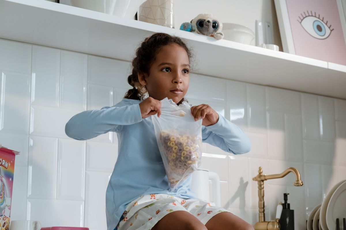 Photo by cottonbro studio on Pexels Junges Mädchen sitzt in der Küche und hält eine Müslitüte in der Hand, bereit zum Frühstück. - Foto von Cottonbro Studio auf Pexels