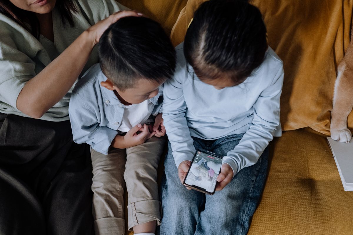 Photo by cottonbro studio on Pexels Two kids sharing a smartphone while sitting with family on a cozy couch. - Photo by cottonbro studio on Pexels