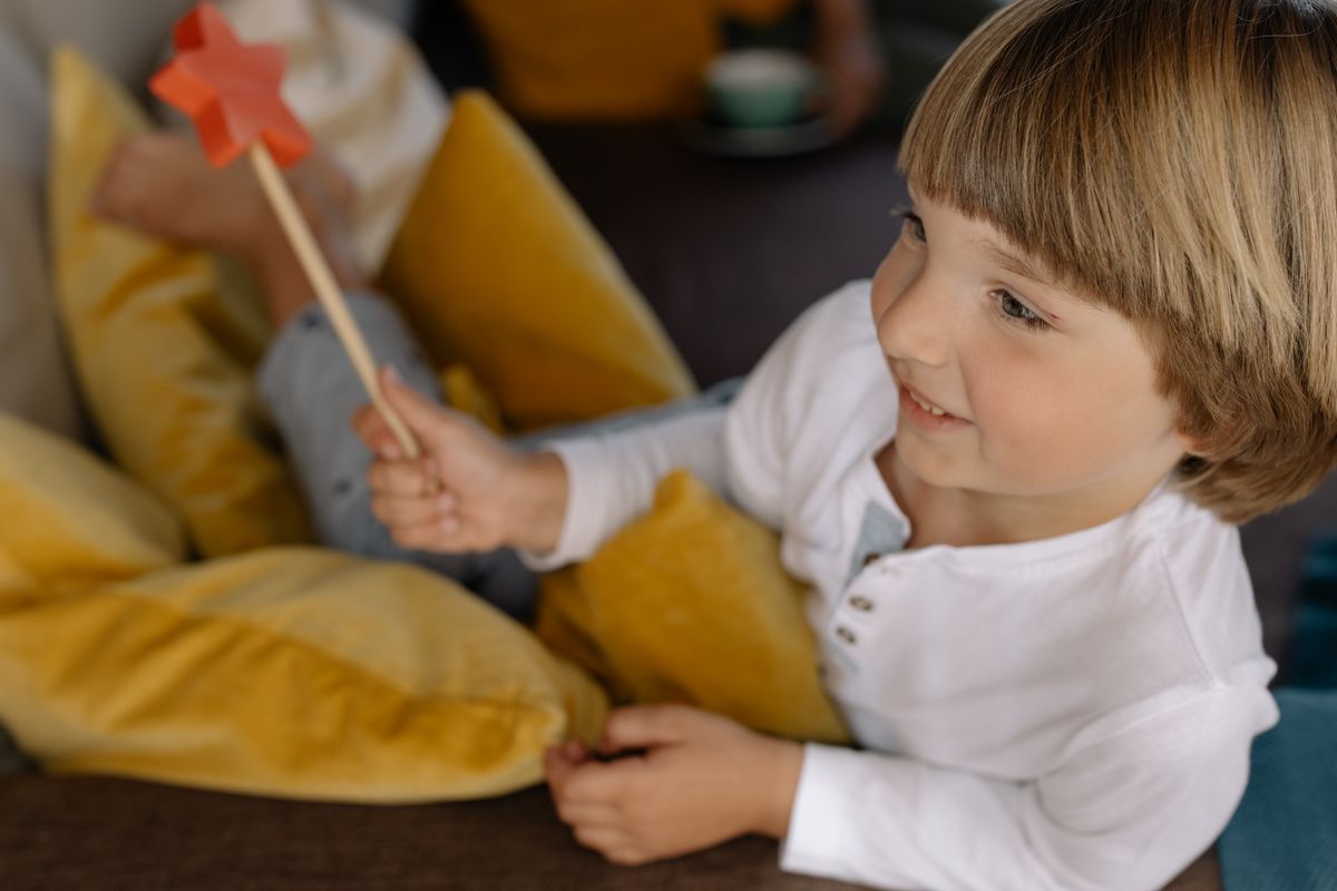 Photo by cottonbro studio on Pexels Cheerful child smiling while holding a red star-shaped wand surrounded by yellow pillows indoors. - Photo by cottonbro studio on Pexels