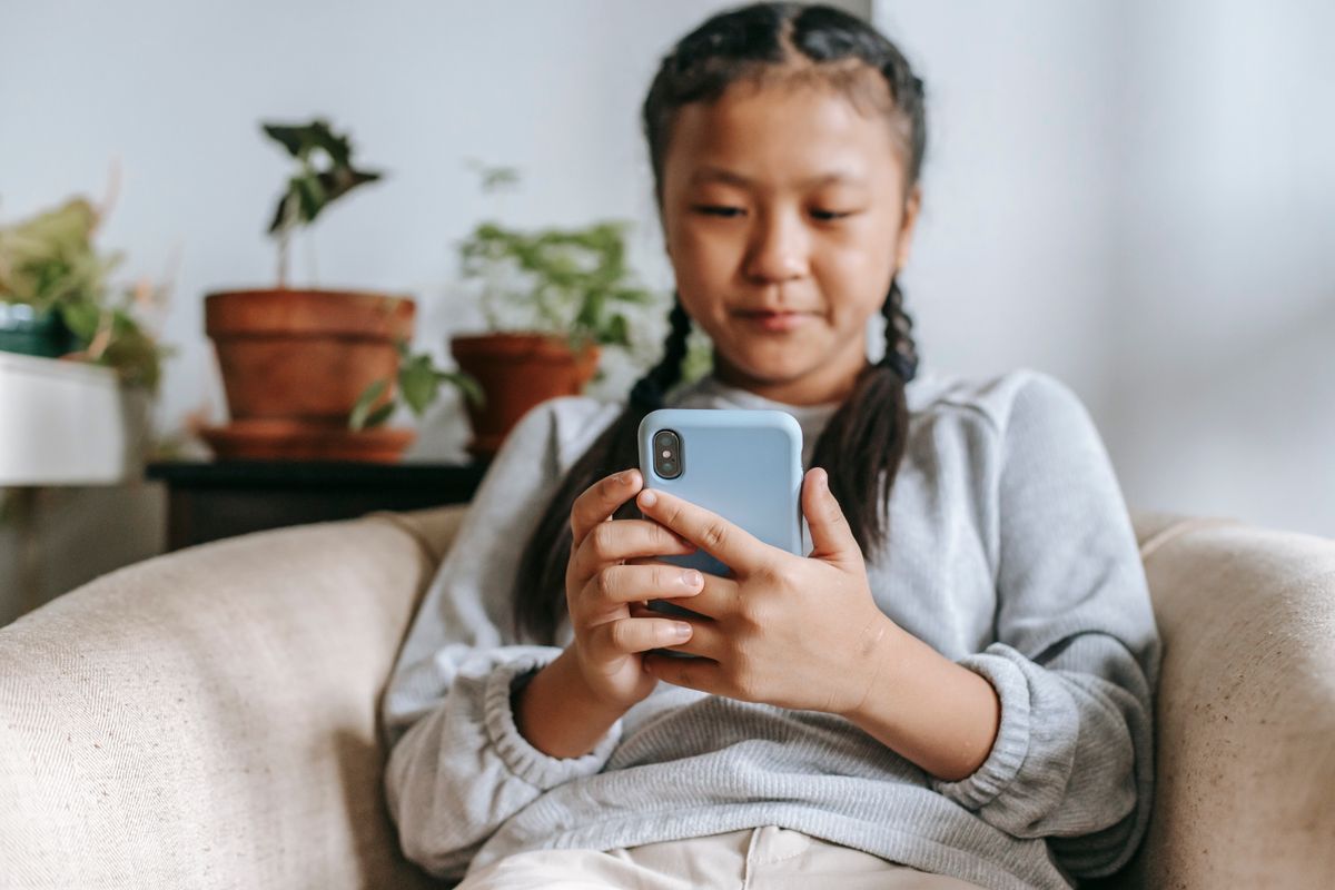Focused Asian girl in casual clothes sitting on cozy armchair and browsing social media on smartphone Focused Asian girl in casual clothes sitting on cozy armchair and browsing social media on smartphone