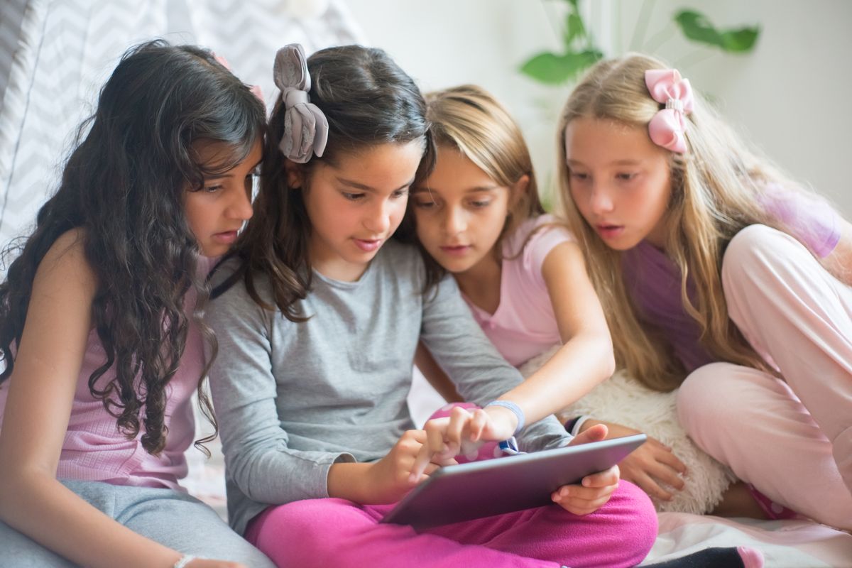 Photo by Kampus Production on Pexels Four young girls sitting together, engaged and focused on a tablet in a cozy indoor setting. - Photo by Kampus Production on Pexels