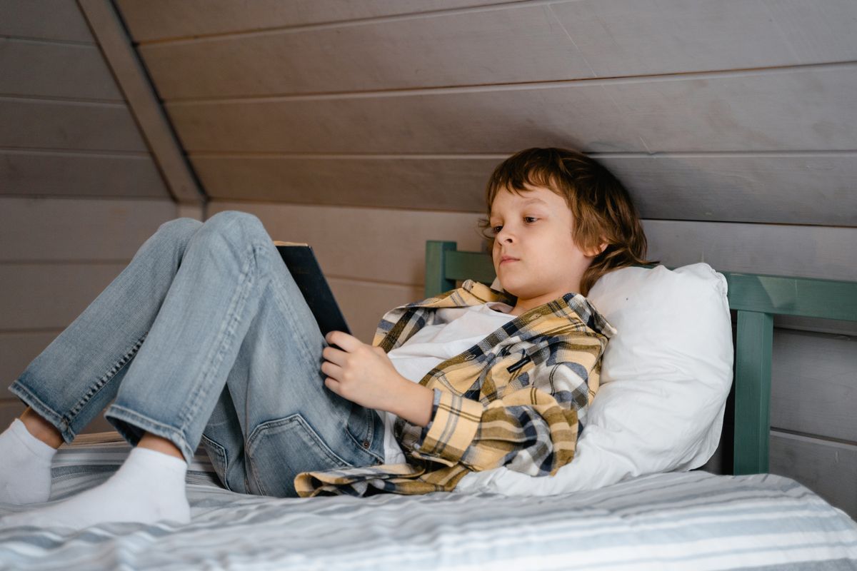 Photo by MART PRODUCTION on Pexels Ein kleiner Junge liegt auf einem Bett und liest ein Buch in einem gemütlichen Schlafzimmer mit Holzmotiv. - Foto von MART PRODUCTION auf Pexels