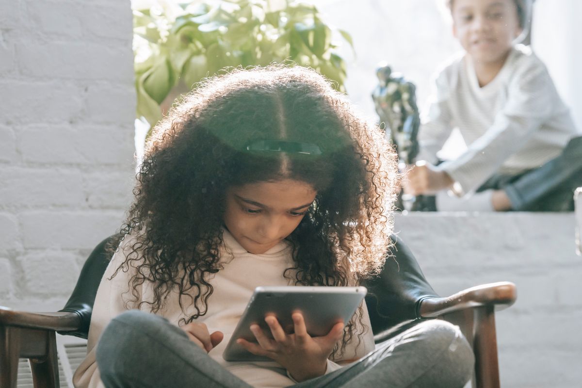 Photo by Marta Wave on Pexels Concentrated African American kid with long curly hair watching video on tablet sitting on comfortable armchair near crop smiling little brother playing with toy - Photo by Marta Wave on Pexels