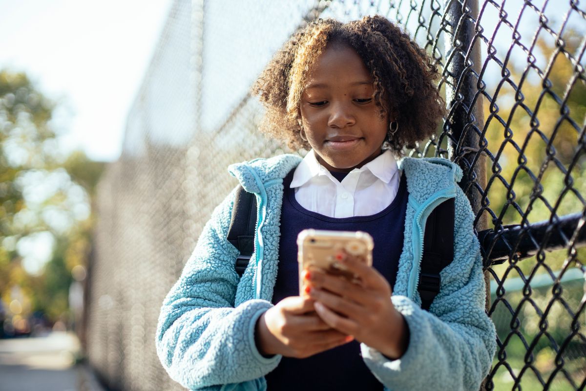 Photo by Mary Taylor on Pexels Positives afroamerikanisches Schulmädchen in blauer Jacke, das an einem sonnigen Herbsttag in der Nähe eines Maschendrahtzauns steht und auf seinem Handy surft – Foto von Mary Taylor auf Pexels