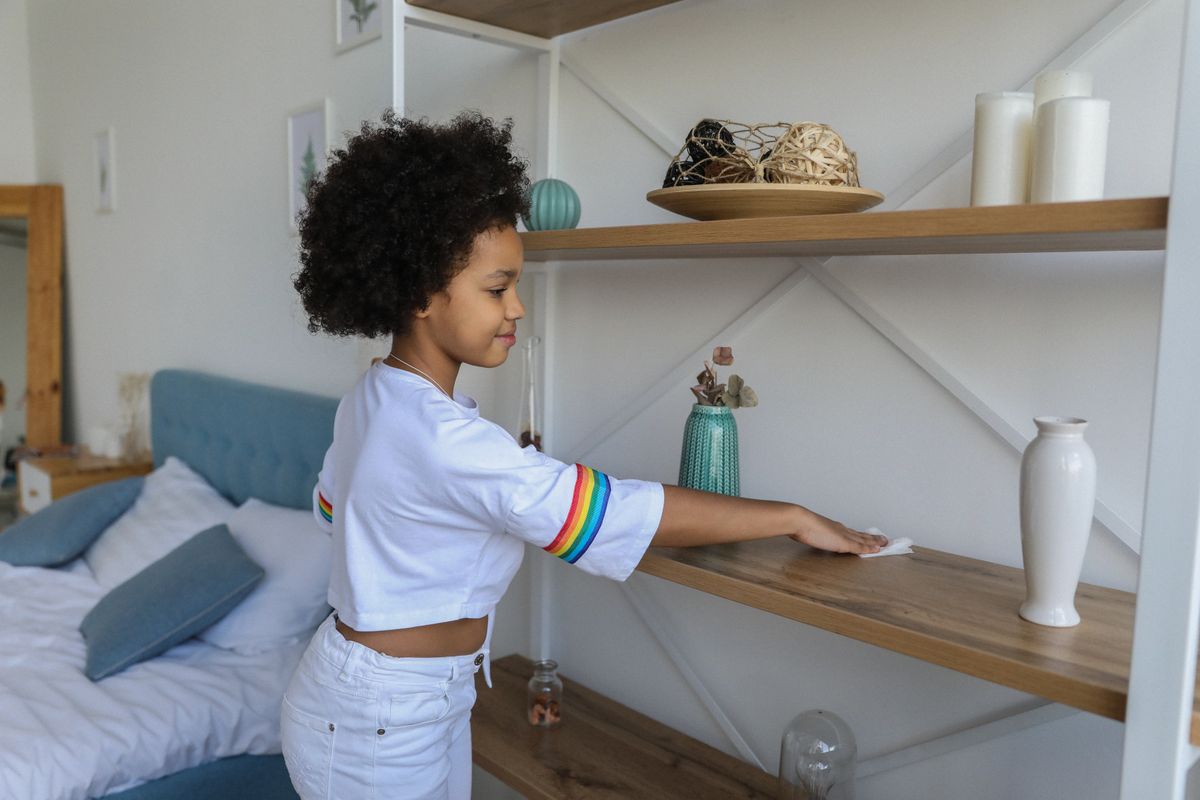 Photo by Monstera Production on Pexels Charmantes afroamerikanisches Mädchen wischt zu Hause Staub vom Holzregal eines Regals – Foto von Monstera Production auf Pexels