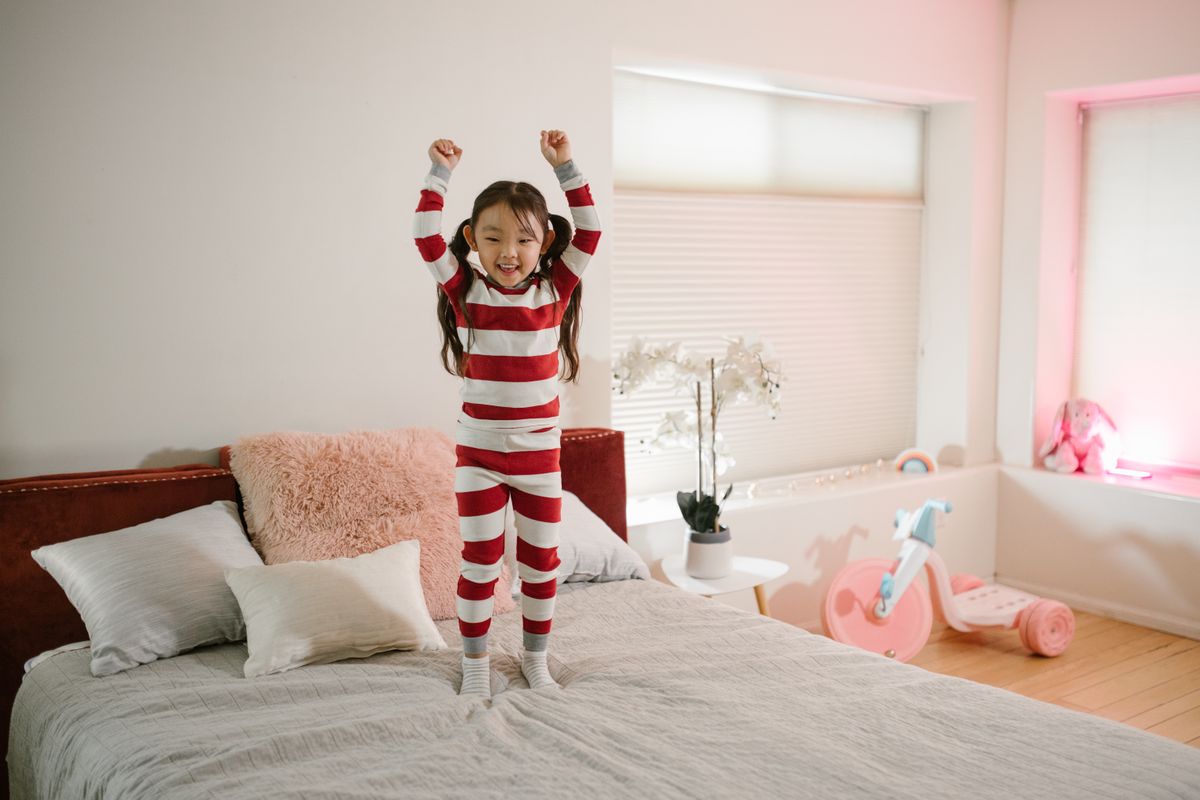 Photo by RDNE Stock project on Pexels Ein fröhliches Kind im gestreiften Pyjama, das in einem hellen und gemütlichen Schlafzimmer auf ein Bett springt. - Foto von RDNE Stock-Projekt auf Pexels