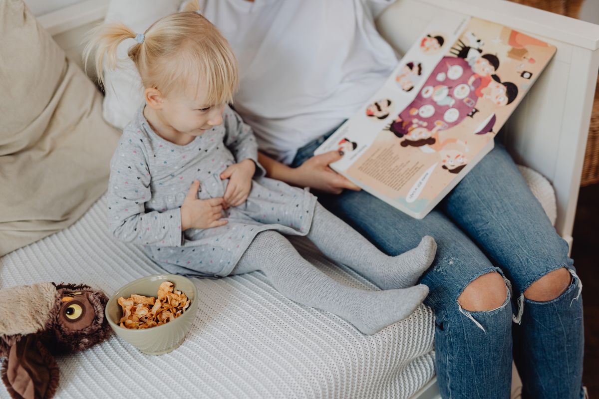 Photo by www.kaboompics.com on Pexels Mother reading a book to her daughter in a cozy bedroom setting with snacks nearby. - Photo by www.kaboompics.com on Pexels