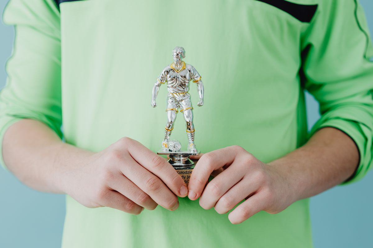 Photo by www.kaboompics.com on Pexels A person holding a silver soccer trophy against a blue background. - Photo by www.kaboompics.com on Pexels