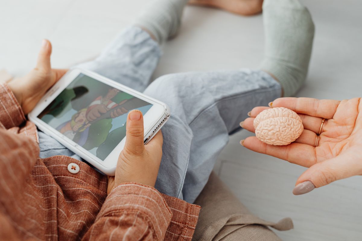 Photo by www.kaboompics.com on Pexels A child watches a cartoon on a tablet as an adult holds a brain model. - Photo by www.kaboompics.com on Pexels