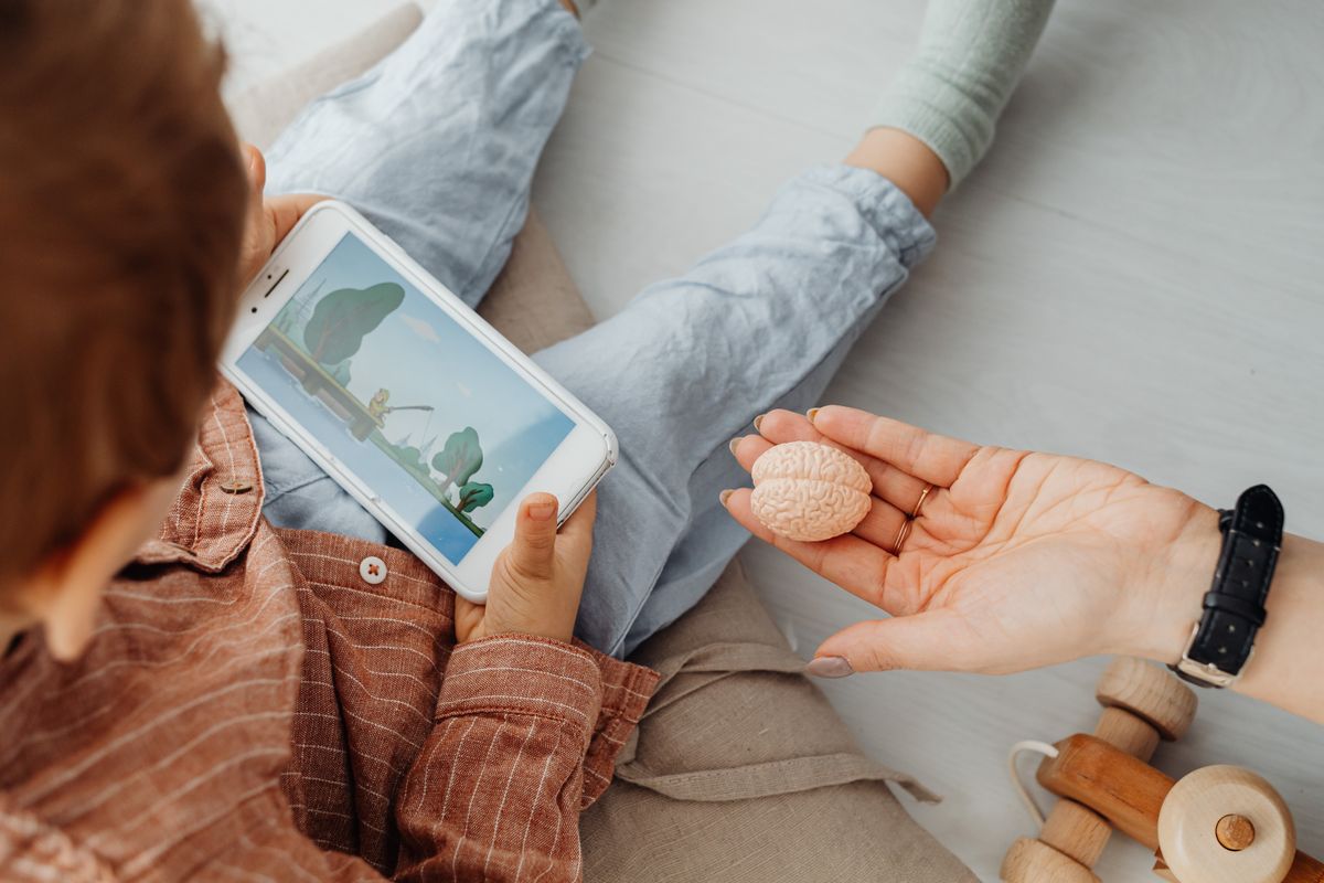 Photo by www.kaboompics.com on Pexels Young child engrossed in a smartphone video while holding a brain model indoors. - Photo by www.kaboompics.com on Pexels